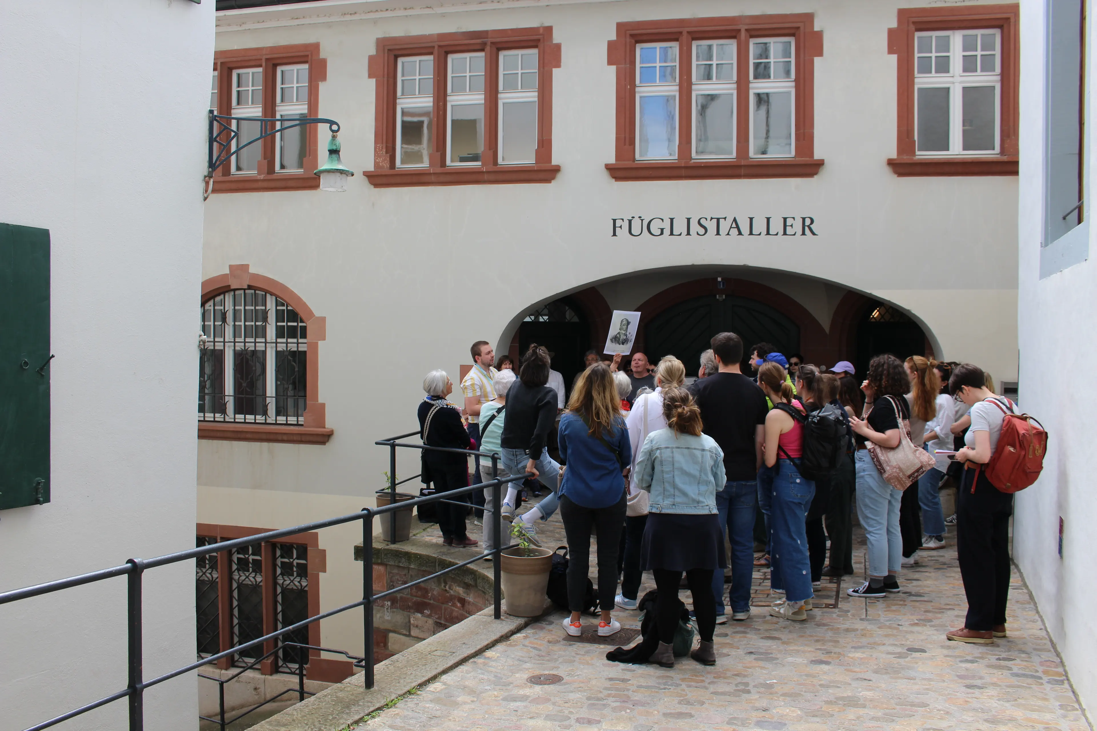 Gruppe von Zuschauer*innen hört sich die Station zu Ganamee an. Die Gruppe steht nahe zusammen in der Altstadt.